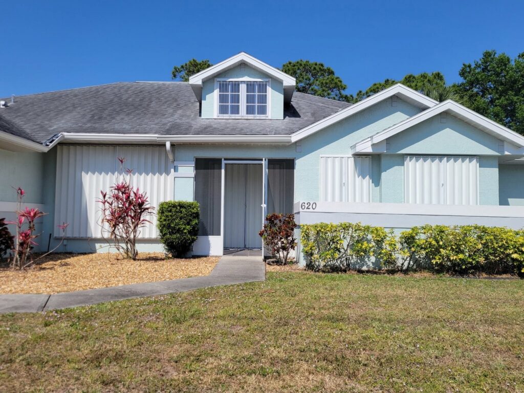 White accordion hurricane shutters installed across the front openings of a blue Florida home