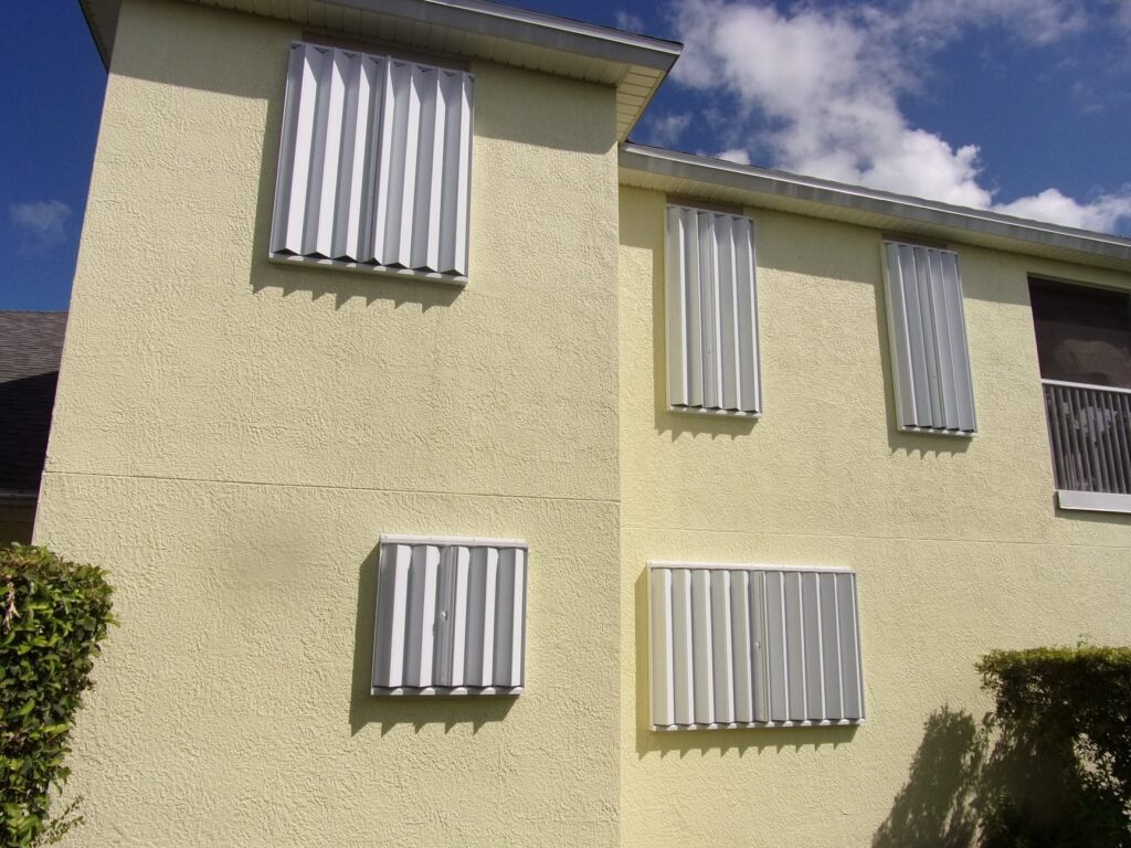 White accordion shutters installed across upper and lower openings on a two-story home