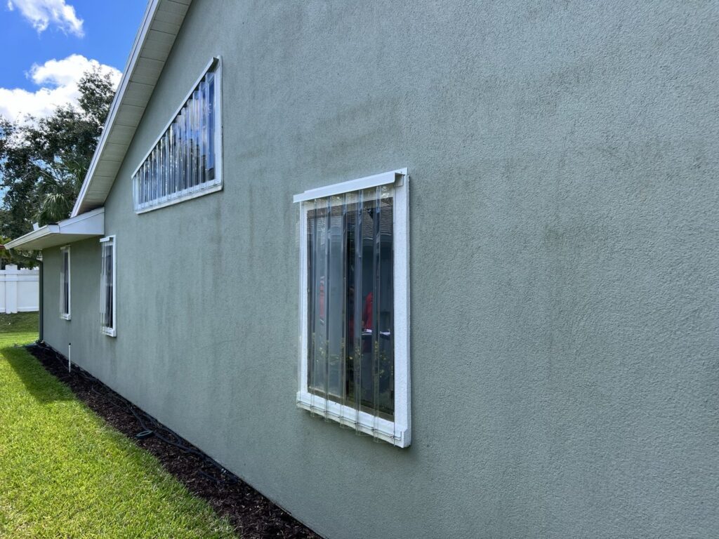 Clear Lexan storm panels installed over windows on a gray stucco home