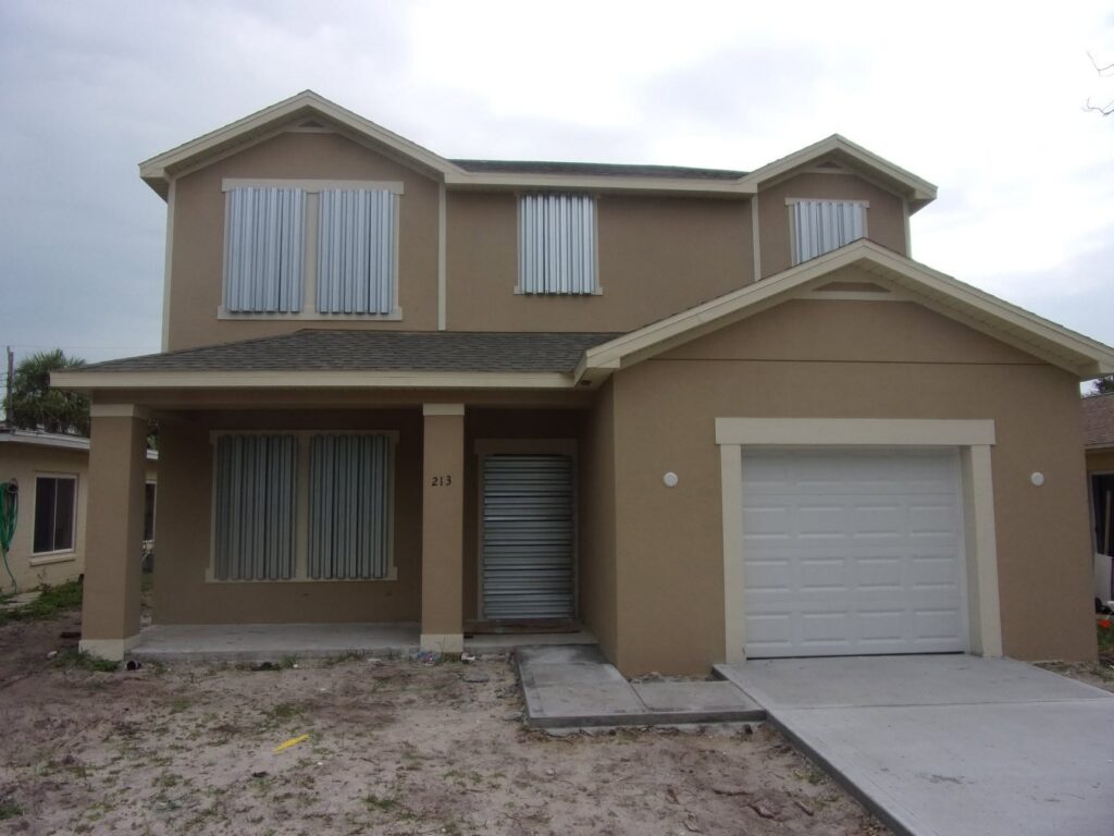 Removable storm panels installed on upper and lower openings of a tan new-construction home