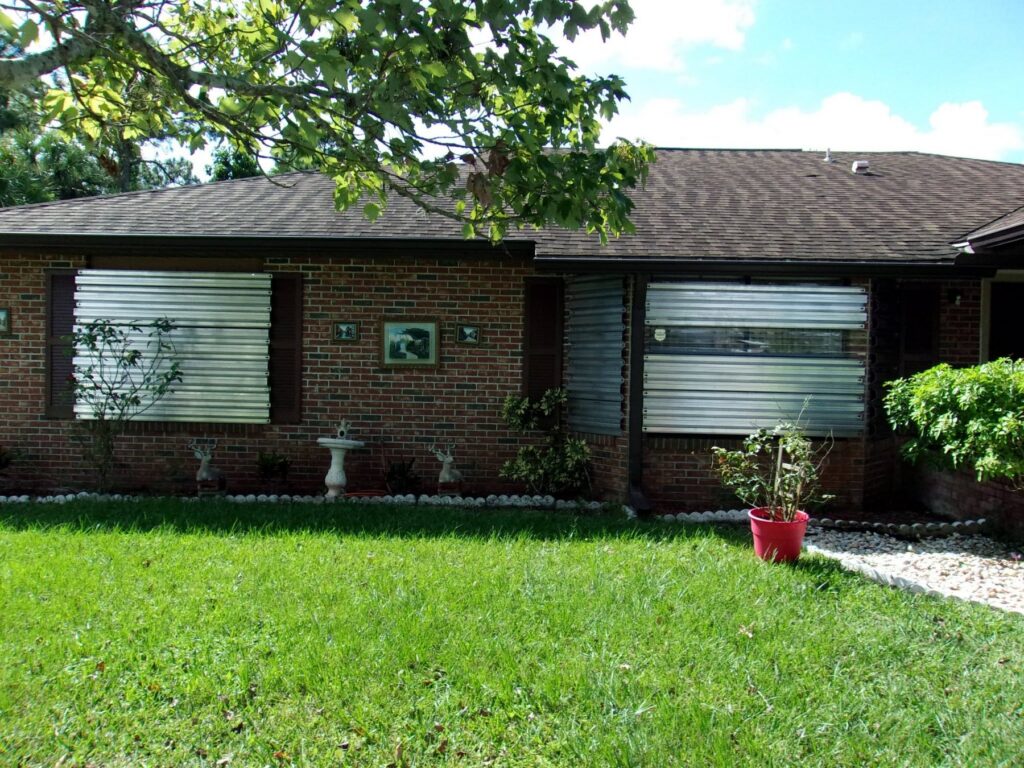 Removable metal storm panels installed across openings on a brick Florida home